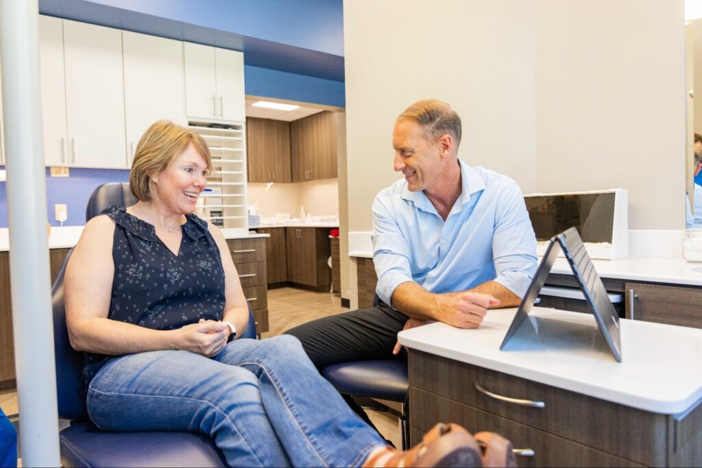 Patient consultation at Jensen Orthodontic Arts, featuring a smiling woman and Dr. Douglas Jensen discussing orthodontic treatment options in a modern office setting.